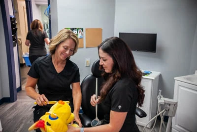 hygienists at All Smiles Dental showing how brushing teeth works on a stuffed animal